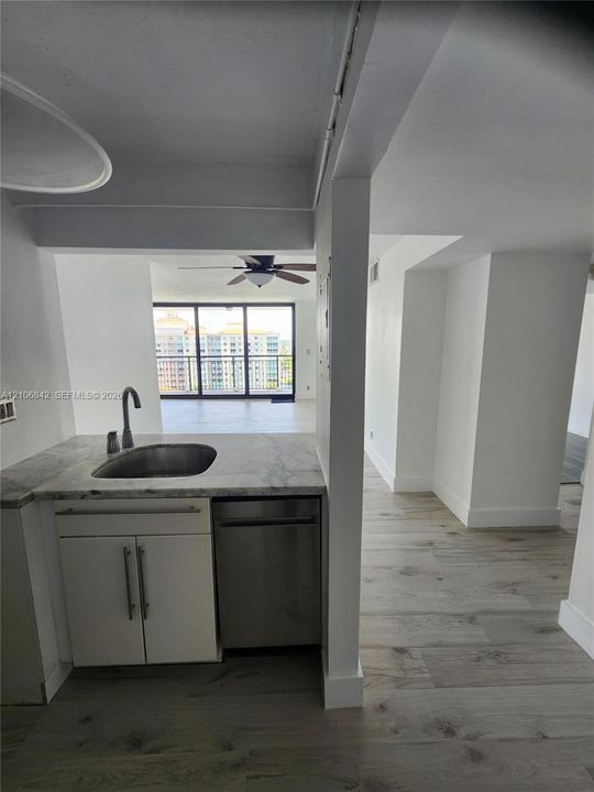 Kitchenette featuring stone-finish countertops, stainless steel sink, under-counter stainless steel dishwasher, and wood-finish flooring