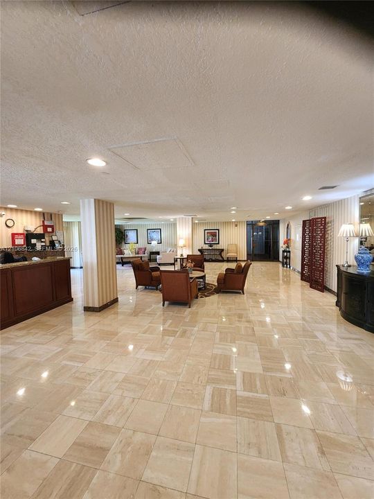 Expansive lobby featuring polished stone tile flooring, built-in reception desk with wood-veneer finish, recessed lighting, and vertical-stripe wall coverings