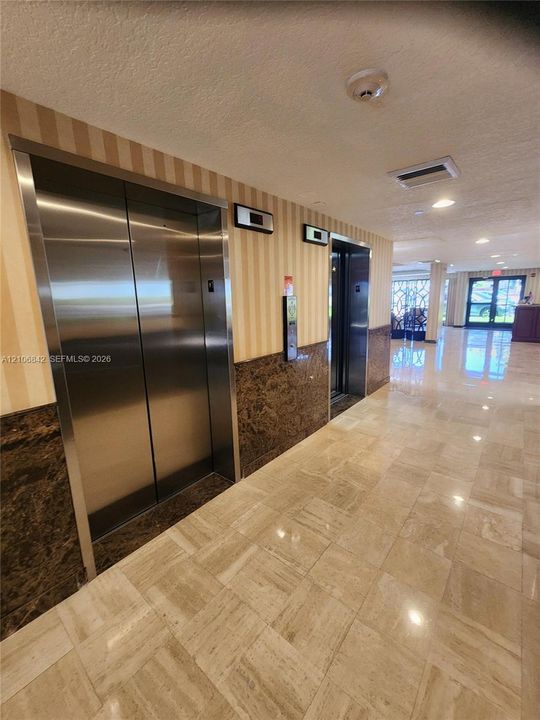 Lobby featuring dual stainless steel elevators, polished stone tile flooring, and decorative stone wainscoting