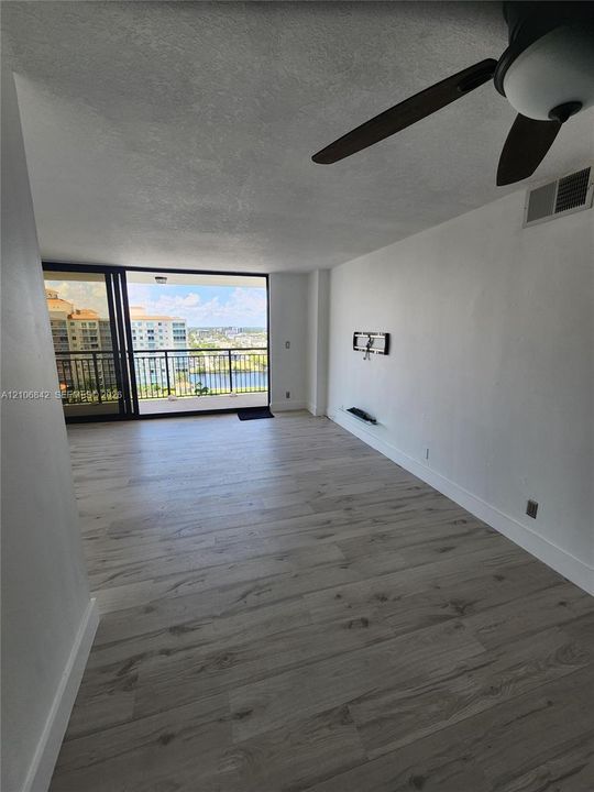 Interior space featuring wood-finish flooring, ceiling fan, and sliding glass doors leading to a balcony with water and building scenery