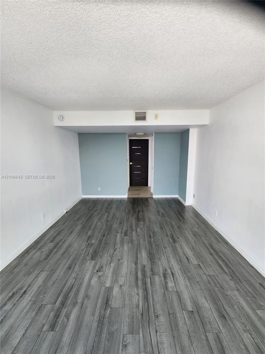 Interior room featuring wood-finish flooring, textured ceiling, and a dark-toned door with horizontal panel detailing