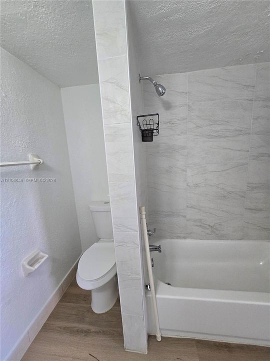 Bathroom featuring a porcelain-tiled shower surround, integrated bathtub, wall-mounted toilet, and wood-finish flooring