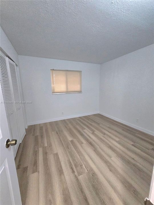 Neutral-toned wood-finish flooring, white walls, and a built-in closet with louvered doors