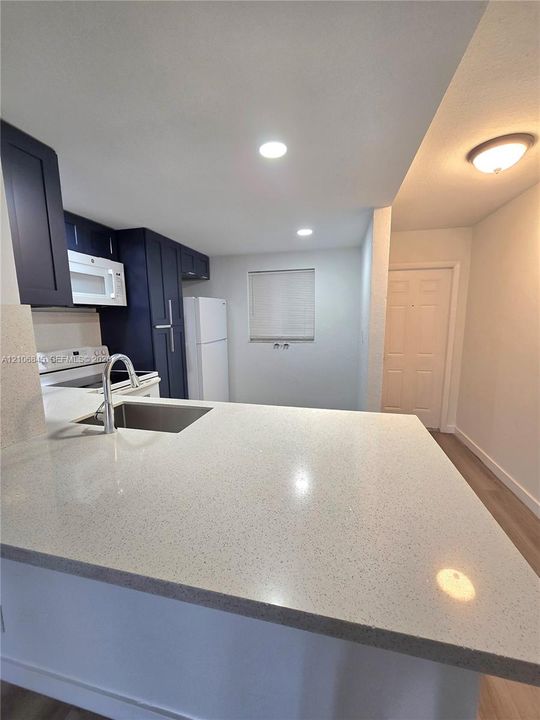 Kitchen featuring navy blue cabinetry, light-toned stone-finish countertops, stainless steel undermount sink with arched faucet, recessed lighting, and wood-finish flooring