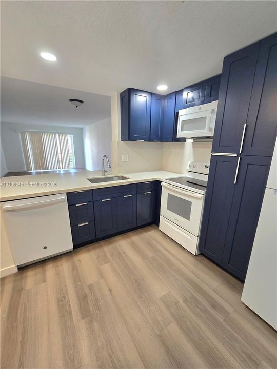 Kitchen featuring blue shaker-style cabinetry, solid-surface countertops, wood-finish flooring, and white built-in appliances