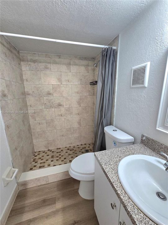 Bathroom featuring a walk-in shower with tile surround, mosaic tile flooring, vanity with stone-finish countertop, integrated sink, and wood-finish flooring