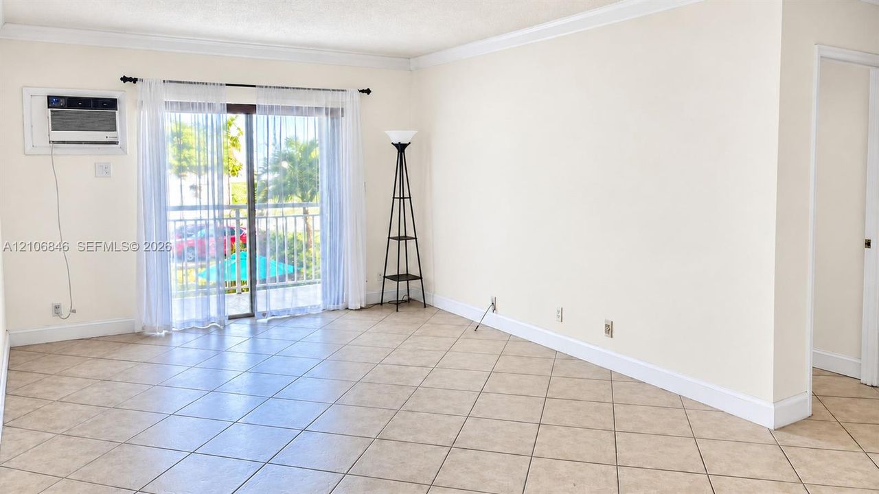Neutral-toned interior featuring ceramic tile flooring, crown molding, and sliding glass doors with balcony access