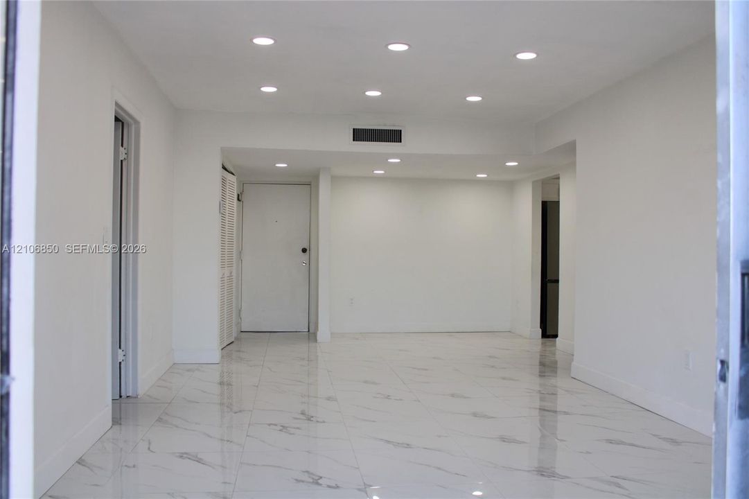 Interior space featuring light-colored stone-finish tile flooring, recessed ceiling lighting, and a white interior door with louvered closet doors