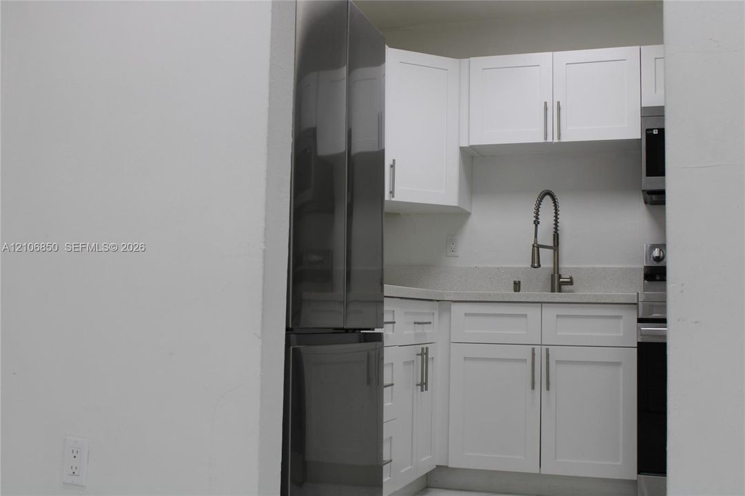 Kitchen featuring white shaker-style cabinetry, stainless steel refrigerator, stone-composite countertop, undermount sink with gooseneck faucet, and stainless steel microwave