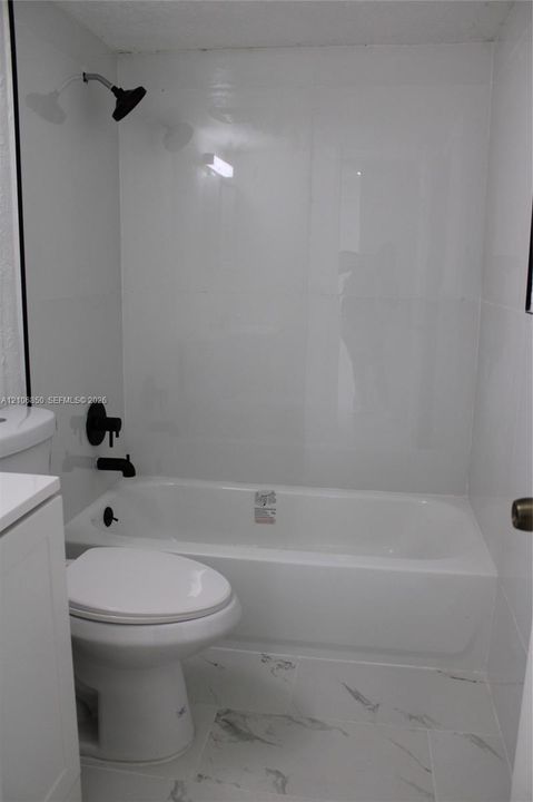 Bathroom featuring a porcelain tub with high-gloss wall surround, matte black rainfall showerhead, matching matte black plumbing fixtures, and patterned tile flooring