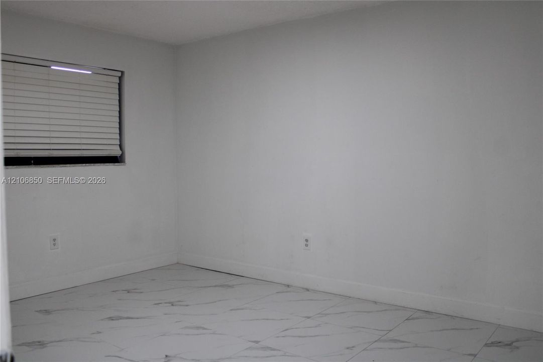 Neutral-toned interior space featuring light-colored tile flooring with a marble-finish pattern and a window equipped with horizontal blinds