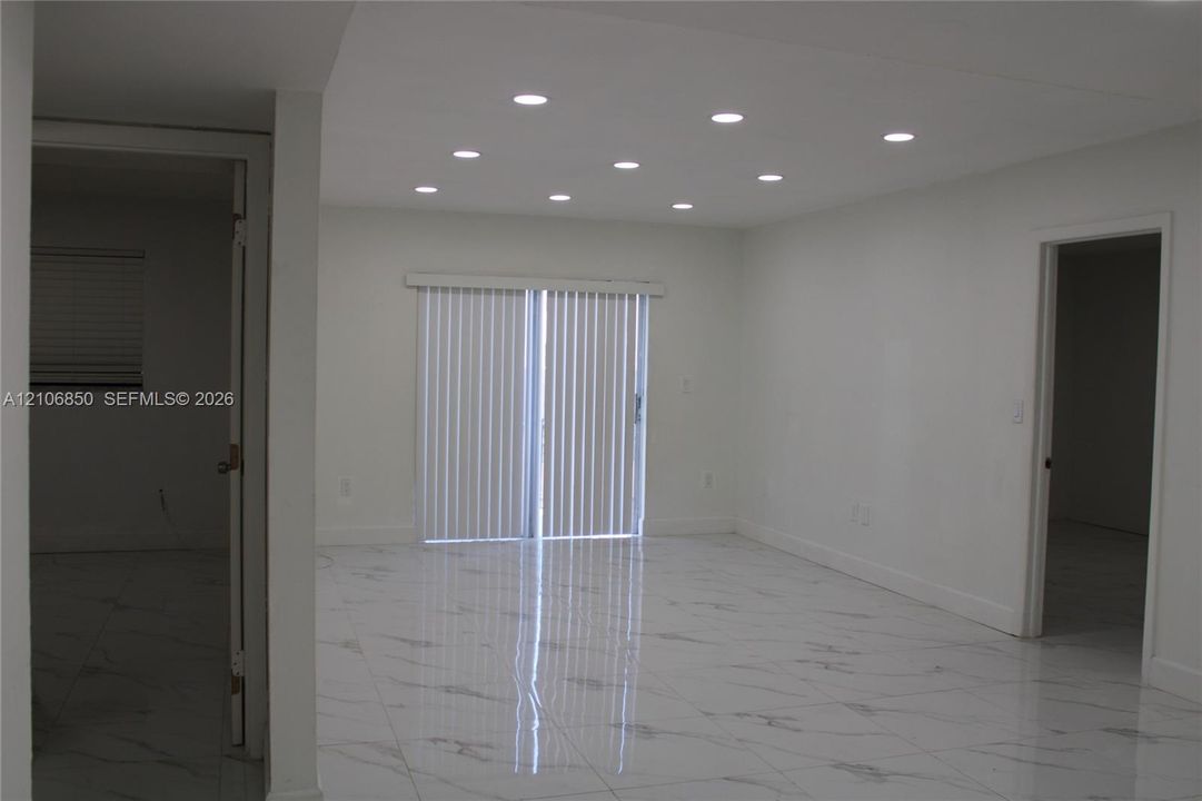 Interior space featuring large-format stone-finish tile flooring, recessed ceiling lighting, and sliding glass doors with vertical blinds