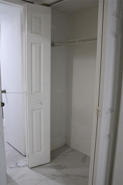 Storage closet featuring bi-fold panel doors and a built-in wire shelf, complemented by large-format stone-patterned tile flooring