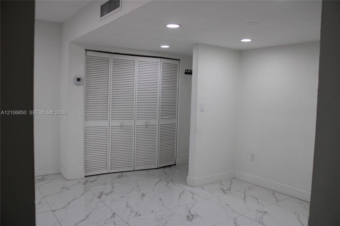 Interior space featuring white stone-finish flooring with grey veining, four-panel louvered closet doors, and recessed ceiling lighting