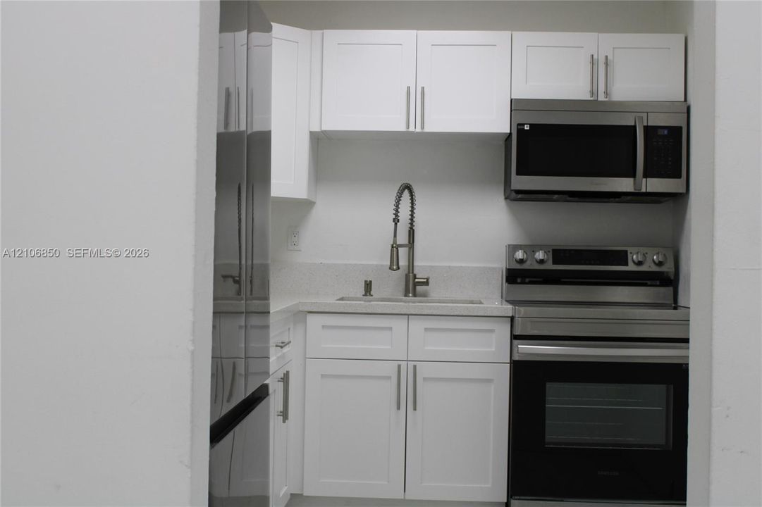 Kitchenette featuring white Shaker-style cabinetry, stainless steel appliances, a stone-composite countertop, and a gooseneck faucet