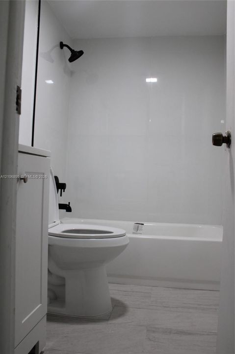 Full bathroom featuring a white bathtub, smooth wall panels, matte black shower head and hardware, and wood-finish flooring