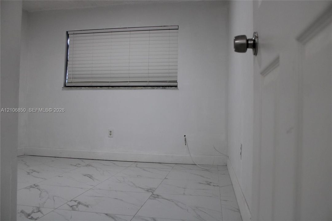 Room featuring white tile flooring with grey veining, neutral wall tones, and a window fitted with horizontal blinds