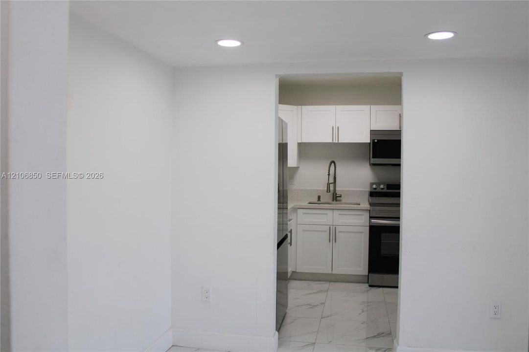 Kitchen featuring white shaker-style cabinetry, stainless steel appliances, a pull-down kitchen faucet, and stone-finish floor tiling with integrated recessed lighting