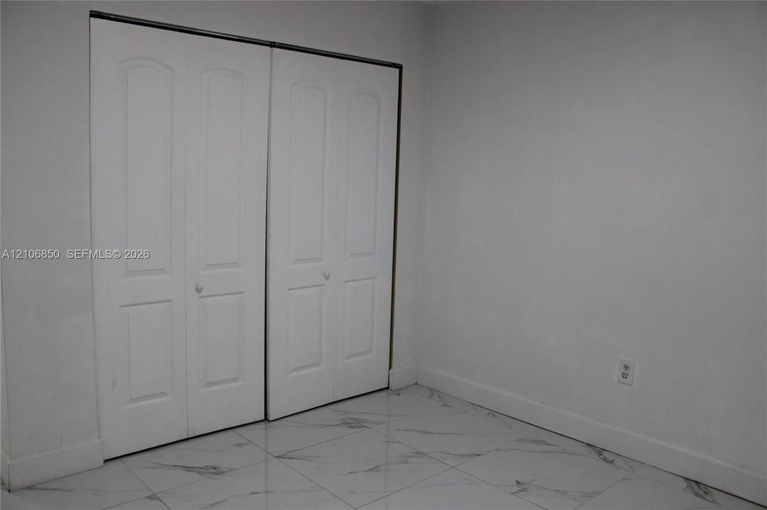 Polished stone-finish flooring with neutral veining and dual white bi-fold closet doors