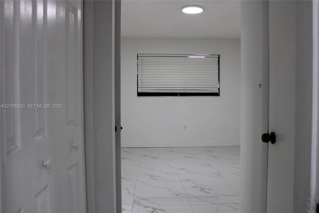 Interior room featuring large-format light-toned tile flooring with veining, multi-panel closet doors, and a window with horizontal blinds