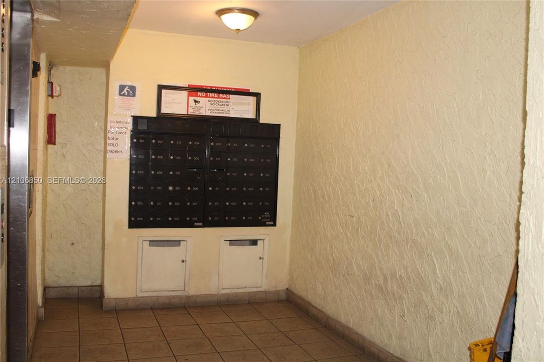 Common area mail center featuring a multi-unit black metal mailbox station, tiled flooring, and a ceiling-mounted light fixture