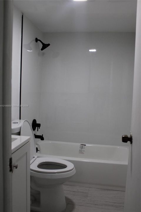 Full bathroom featuring a tub-shower combination with matte black fixtures, white surround, and a vanity cabinet