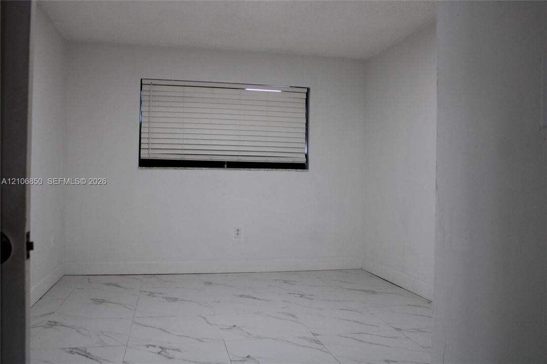 Interior room featuring large-format, white veined tile flooring, neutral wall finishes, and a window with horizontal blinds