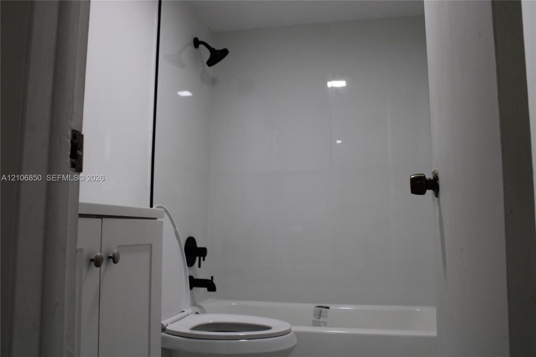 Bathroom featuring white panel shower surround, matte black showerhead and tub faucet, white vanity cabinet with circular pulls, and white standard toilet