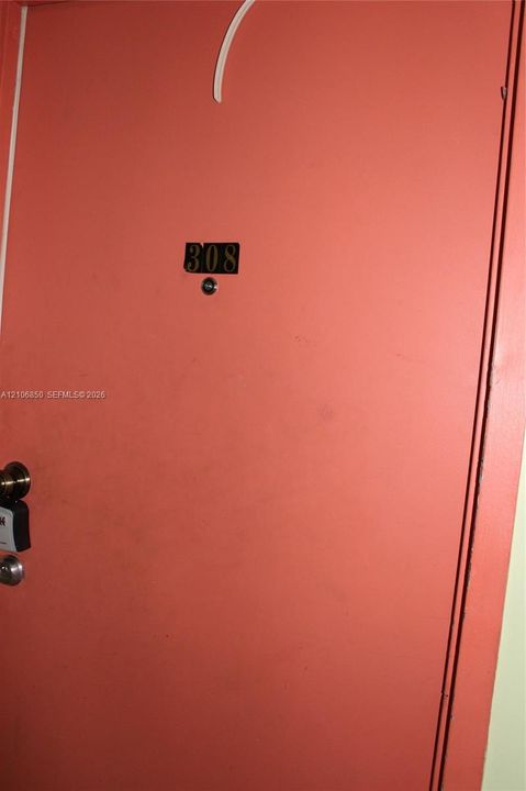 Solid-core entry door featuring a matte finish, brass-toned numerical identification plate, and integrated door viewer