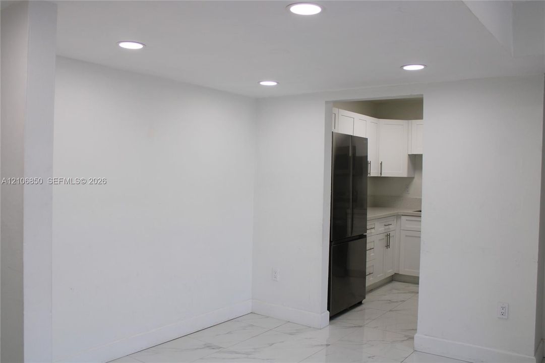 Recessed ceiling lighting, large-format tile flooring, and white Shaker-style cabinetry with neutral countertops and a stainless steel refrigerator