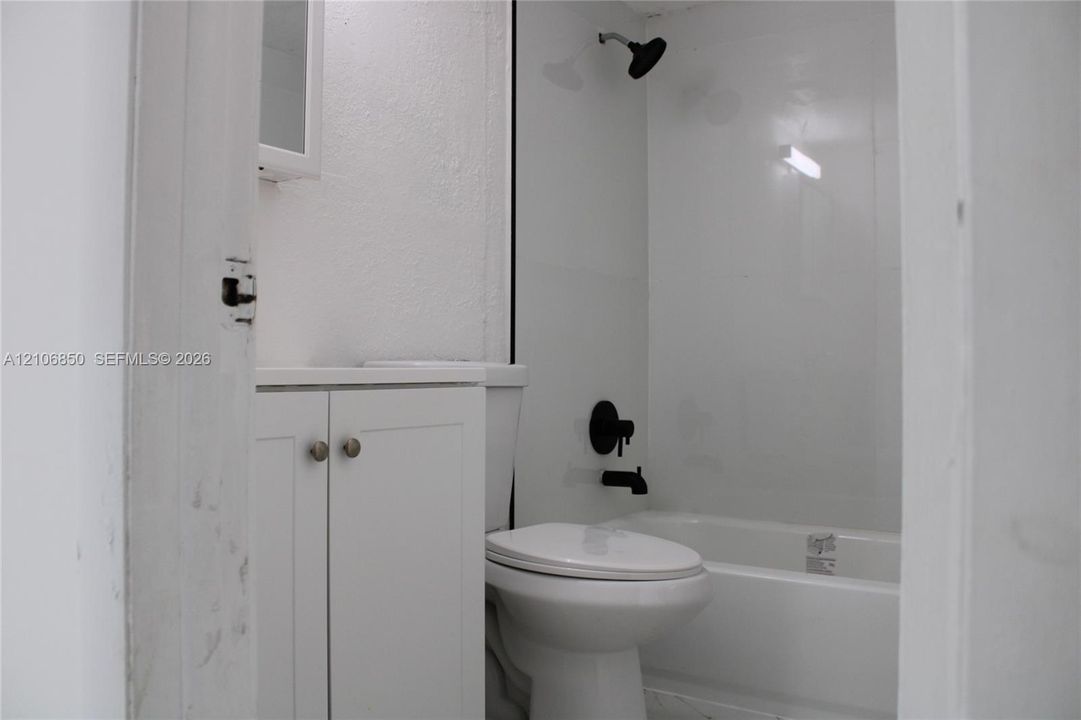 Bathroom featuring white shaker-style cabinetry, matte black hardware, wall-mounted shower head, and a white bathtub surround