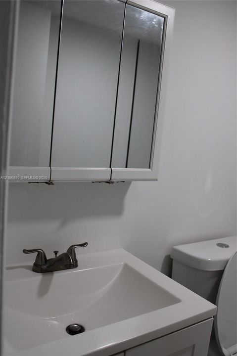 Tri-fold mirrored medicine cabinet, solid-surface vanity countertop with integrated basin, and dual-handle metallic faucet