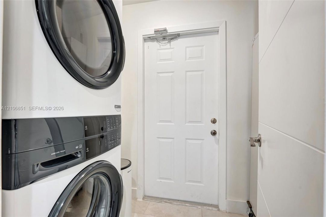 Stacked laundry unit with white finish and integrated control panels, six-panel interior door, and satin-finish metal hardware