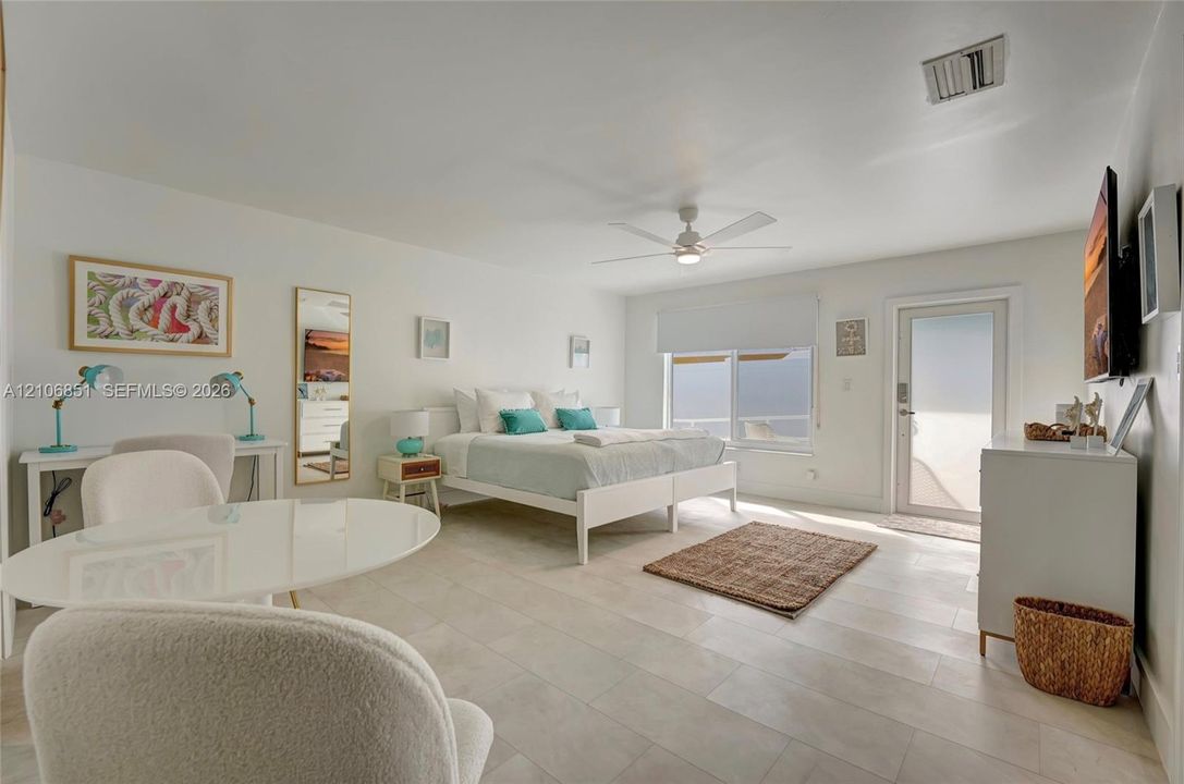 Spacious room featuring large-format stone-tile flooring, a central ceiling fan, expansive windows, and a glass-paneled exterior door