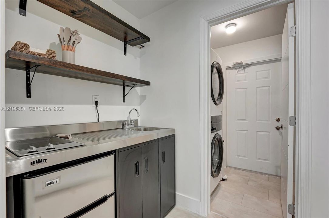 Utility space featuring a stainless steel countertop, integrated sink, built-in cooktop, under-counter refrigerator, and wood-finish wall shelving