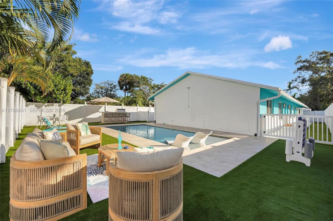 Outdoor recreation area featuring a rectangular swimming pool, stone-paver pool deck, synthetic lawn, and perimeter vinyl fencing
