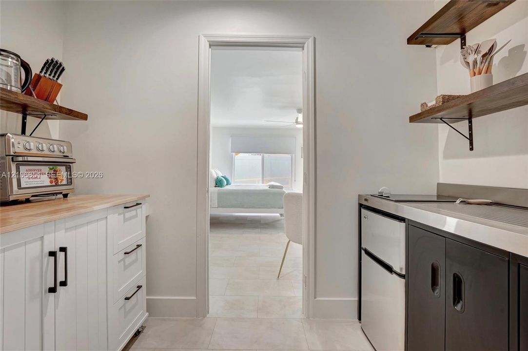Kitchenette featuring white cabinetry with wooden countertops, dark lower cabinets with metal surfacing, and wall-mounted wooden shelving