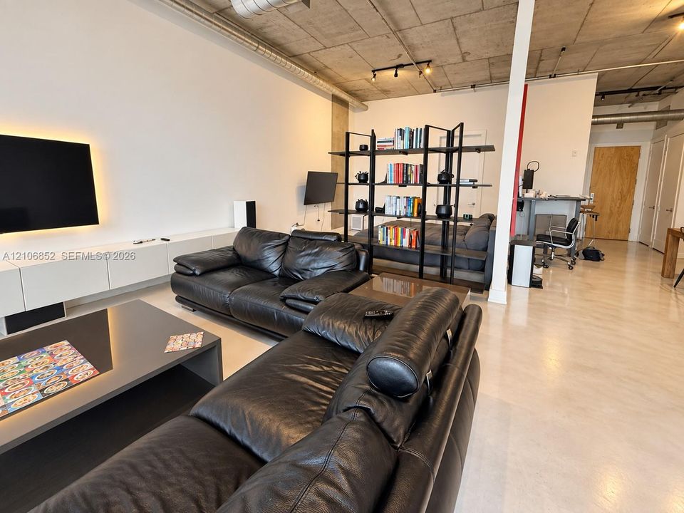 Industrial-style living space featuring an exposed concrete ceiling, polished concrete flooring, built-in wall-mounted cabinetry, and exposed ductwork