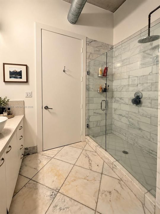 Walk-in shower featuring glass enclosure, subway-tiled surround, and rainfall showerhead, complemented by diagonal-set stone tile flooring and exposed industrial-style ductwork