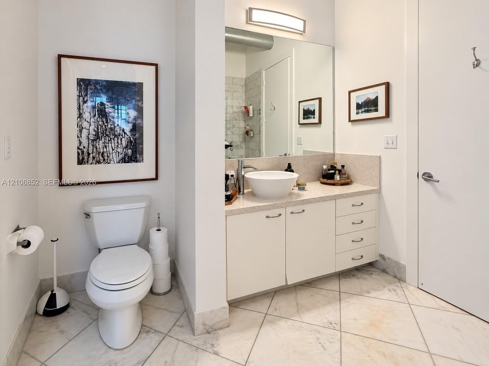 Vanity featuring an integrated cabinet with drawers, solid surface countertop, white vessel sink, and wall-mounted light fixture, paired with stone-finish floor tiling