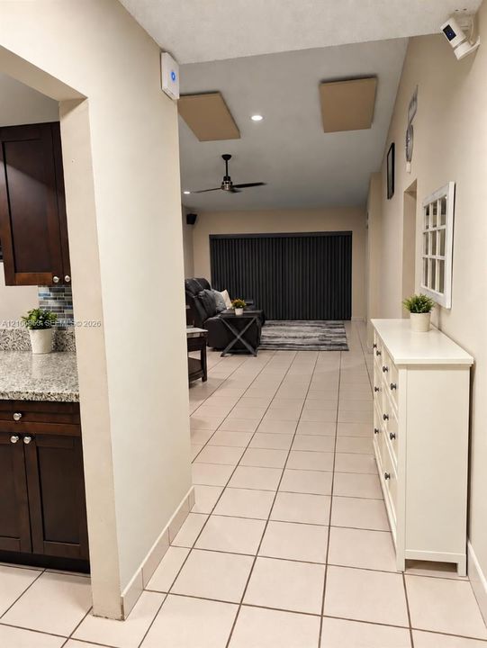 Kitchen featuring dark wood cabinetry, stone-finish countertops, and multi-colored glass tile backsplash, complemented by neutral tile flooring throughout the interior