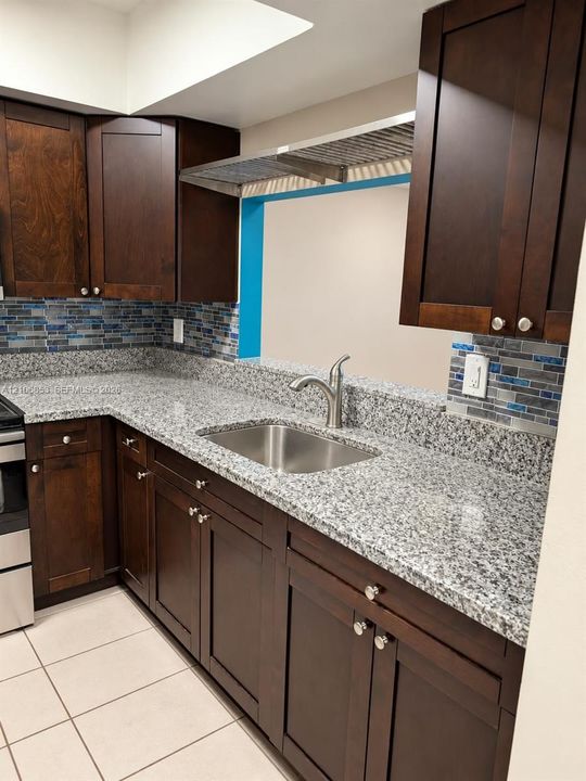 Dark-toned wood cabinetry, stone-surface countertops, stainless steel undermount sink, gooseneck faucet, and mosaic tile backsplash