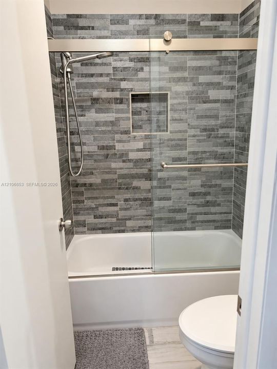 Walk-in shower enclosure featuring stacked stone wall tile, built-in recessed wall niche, sliding glass door, and stainless steel hand-held shower fixture