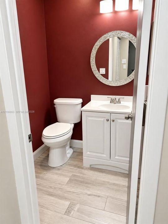 Bathroom featuring a white vanity cabinet with a solid surface countertop, an undermount sink, a circular mosaic-tile framed mirror, and wood-finish tile flooring