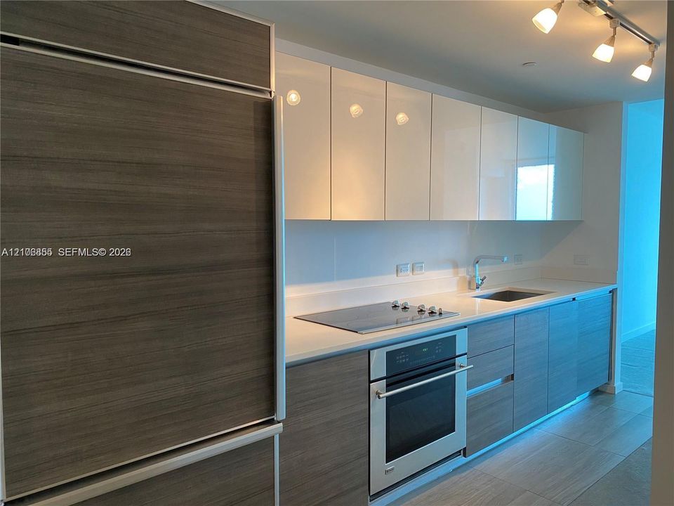 Kitchen featuring high-gloss upper cabinetry, wood-finish lower cabinetry, integrated refrigerator, solid-surface countertops, and stainless steel built-in oven