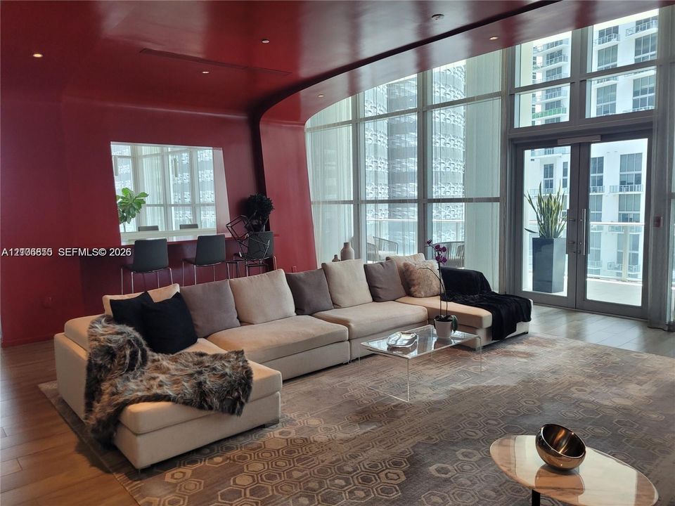 Floor-to-ceiling glass walls, integrated bar with counter seating, high-gloss red accent wall, recessed ceiling lighting, and wood-finish flooring