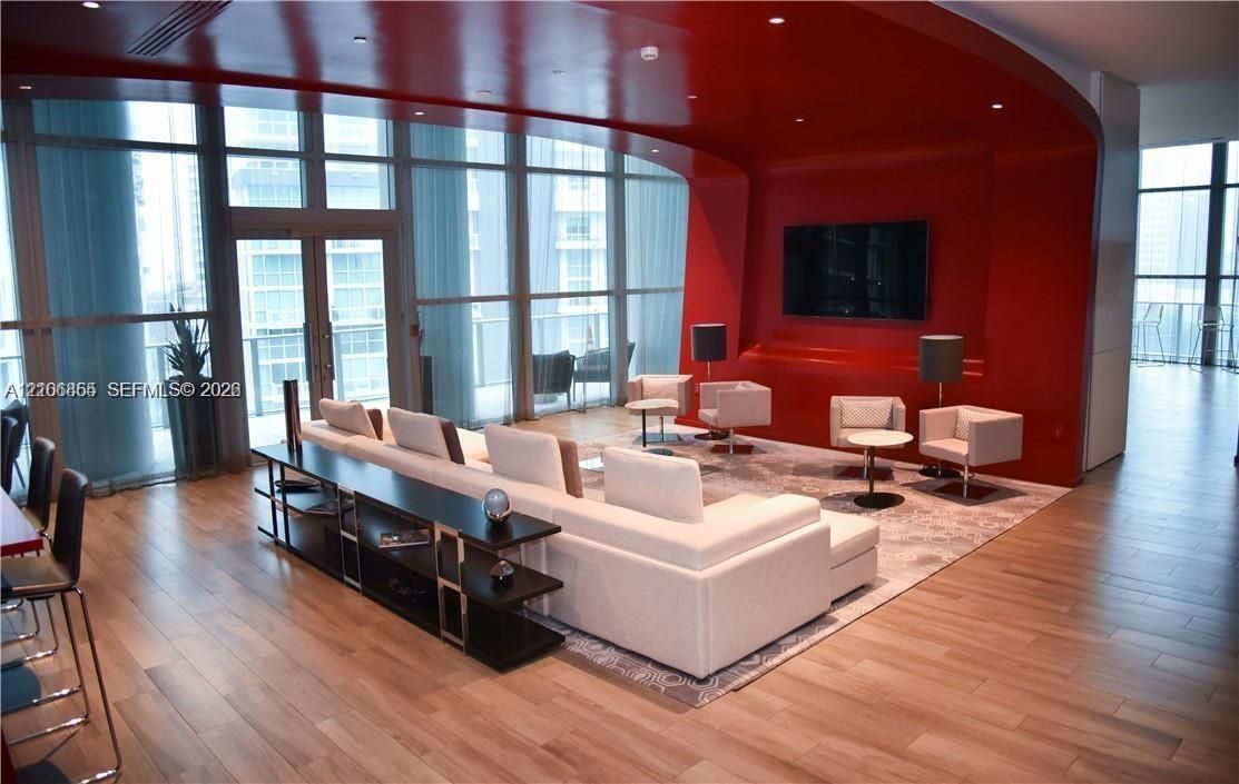 Floor-to-ceiling glass wall, architectural red curved accent wall, recessed ceiling lighting, and wood-finish flooring