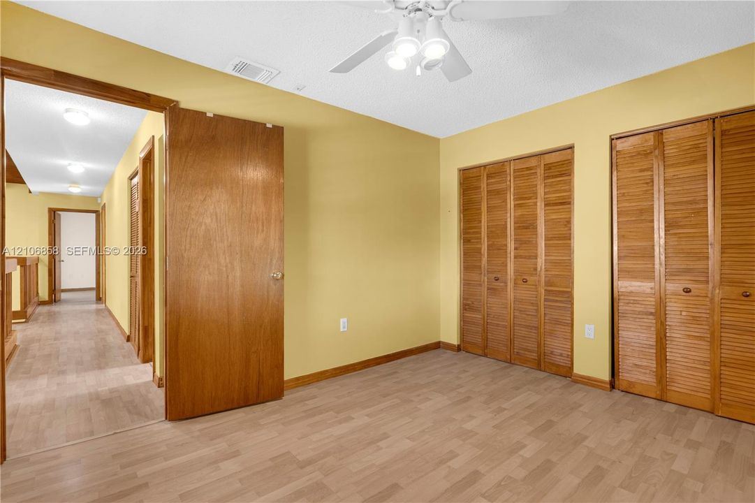 Wood-finish flooring, dual bi-fold wooden closet doors, and a ceiling-mounted light fixture with a fan