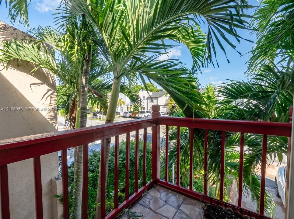 Elevated balcony featuring a red-painted wood balustrade and tiled flooring, framed by mature palm trees