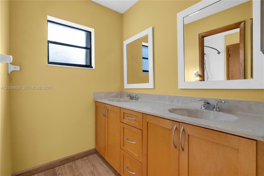 Dual-sink vanity with a solid-surface countertop, wood-finish cabinetry, rectangular framed mirrors, and a window providing natural light